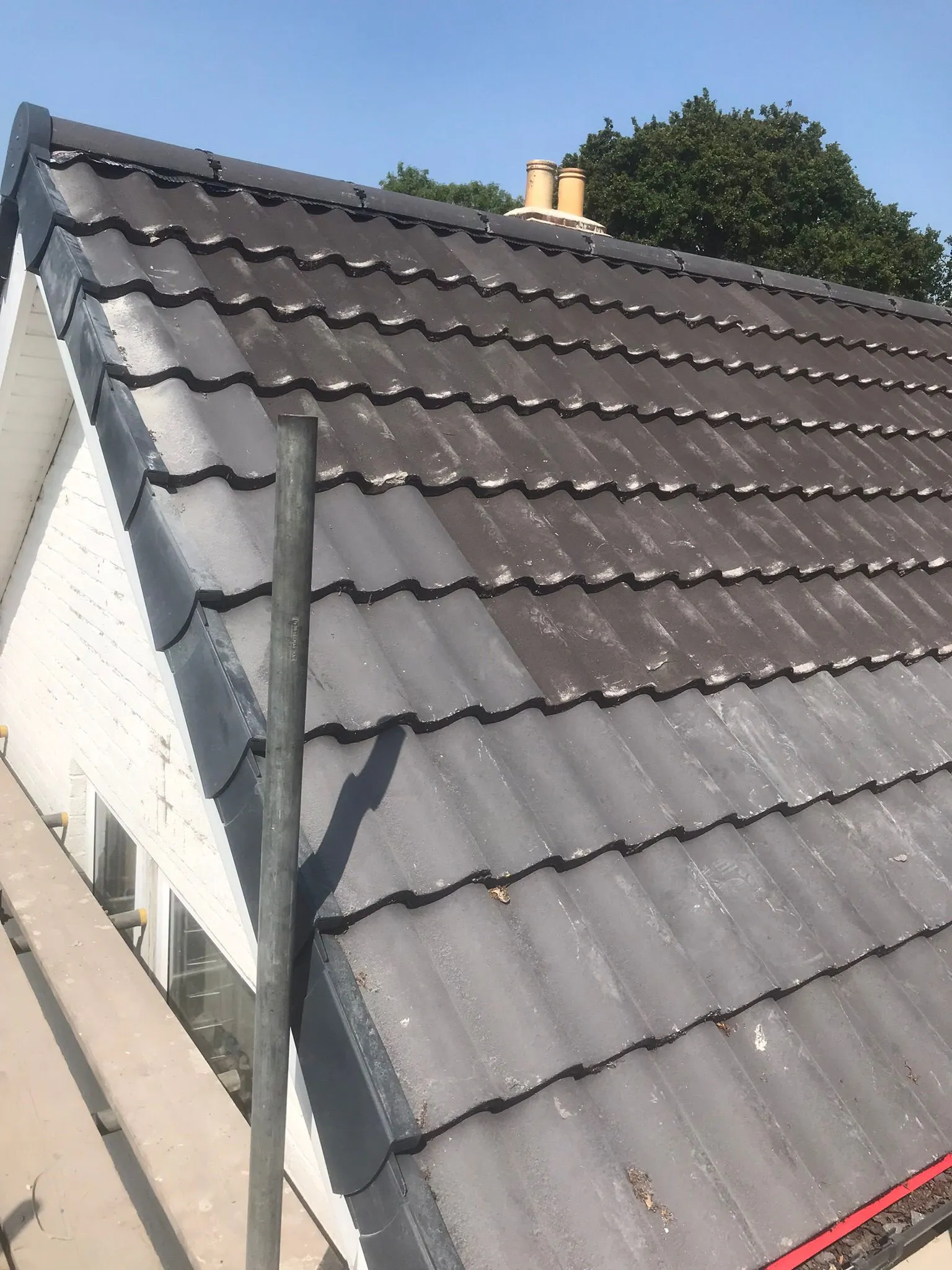 Tiled roof half-cleaned, showing a stark contrast between the cleaned dark grey tiles and the uncleaned, lighter, weathered section.