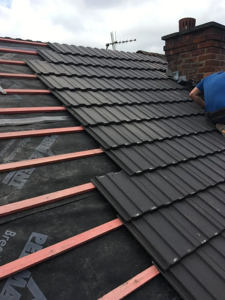 Roofer laying new black roof tiles on a pitched roof