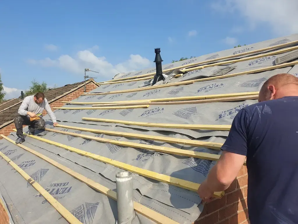 Two roofers installing new roof felt and battens on a house roof