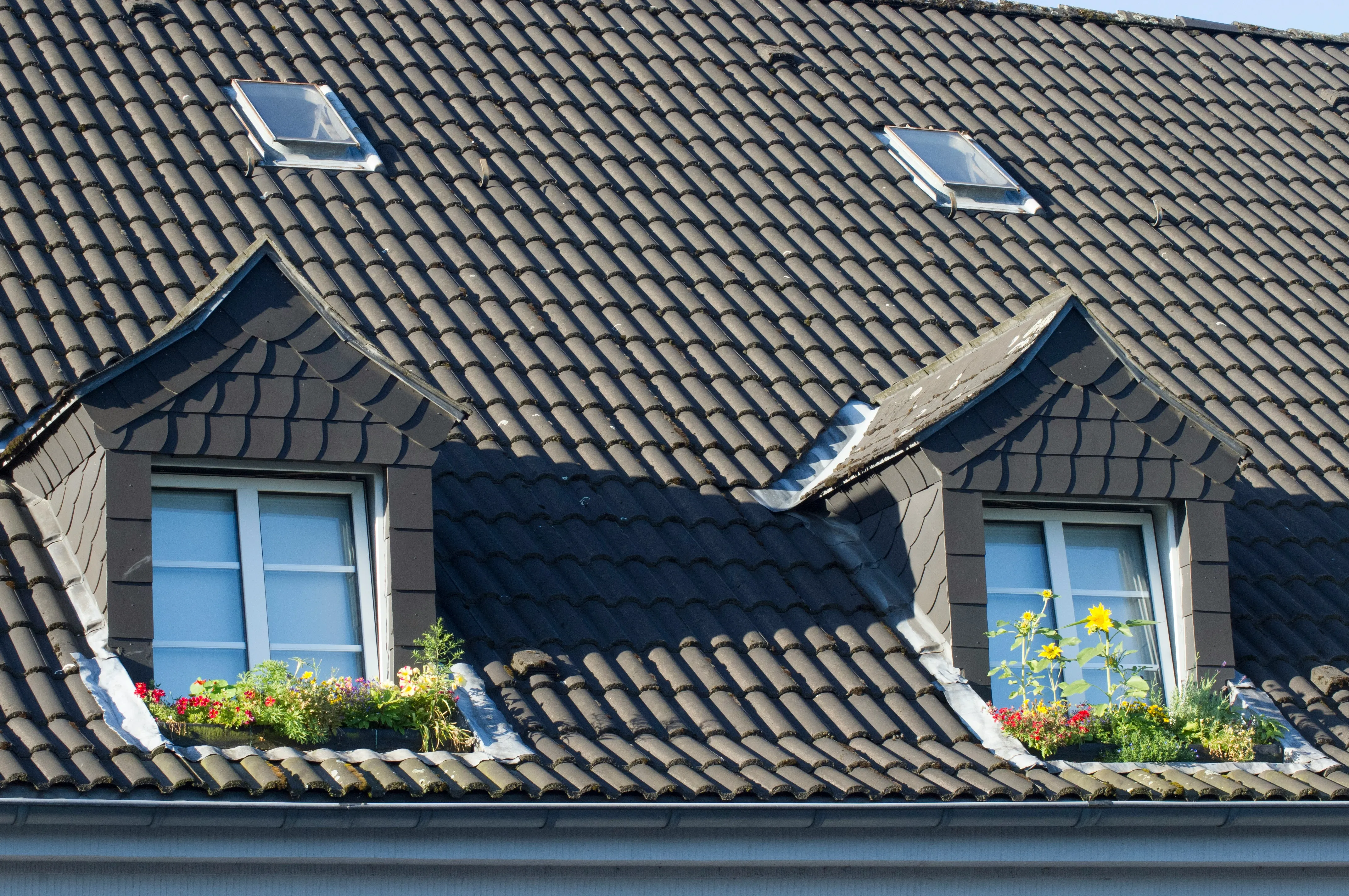 Grey tiled pitched roof with dormer windows and skylights, showcasing residential roofing elements.