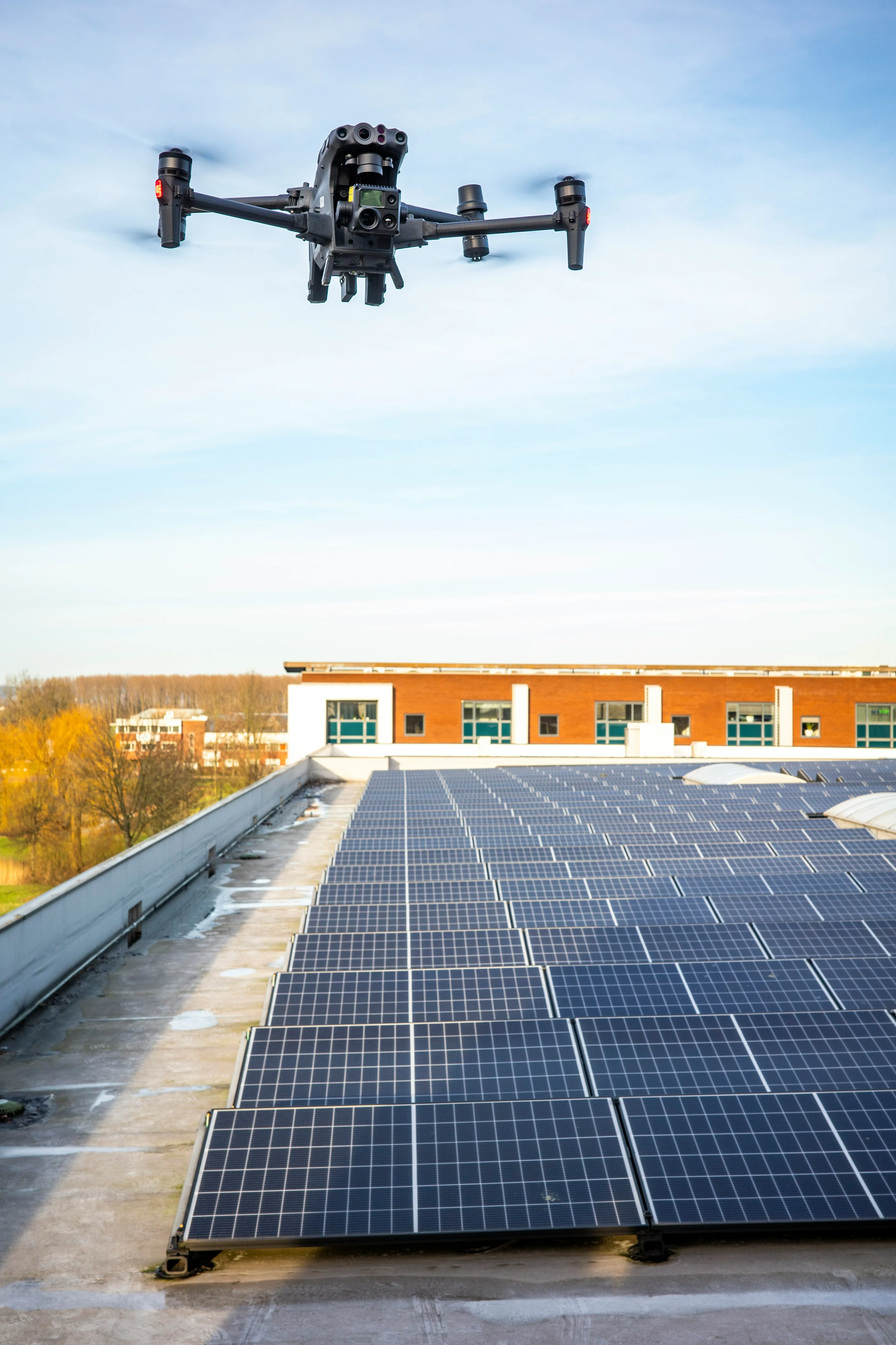 Drone flying over a large flat roof with solar panels, performing a roof inspection.
