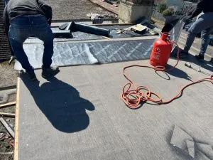 Roofers applying torch-on felt to a flat roof during installation or repair.