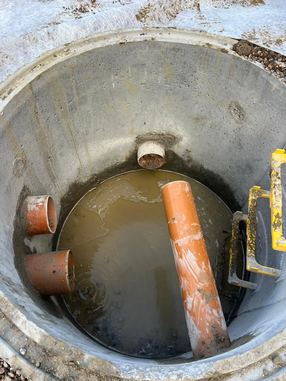 A blocked manhole filled with dirty standing water and various drainage pipes.