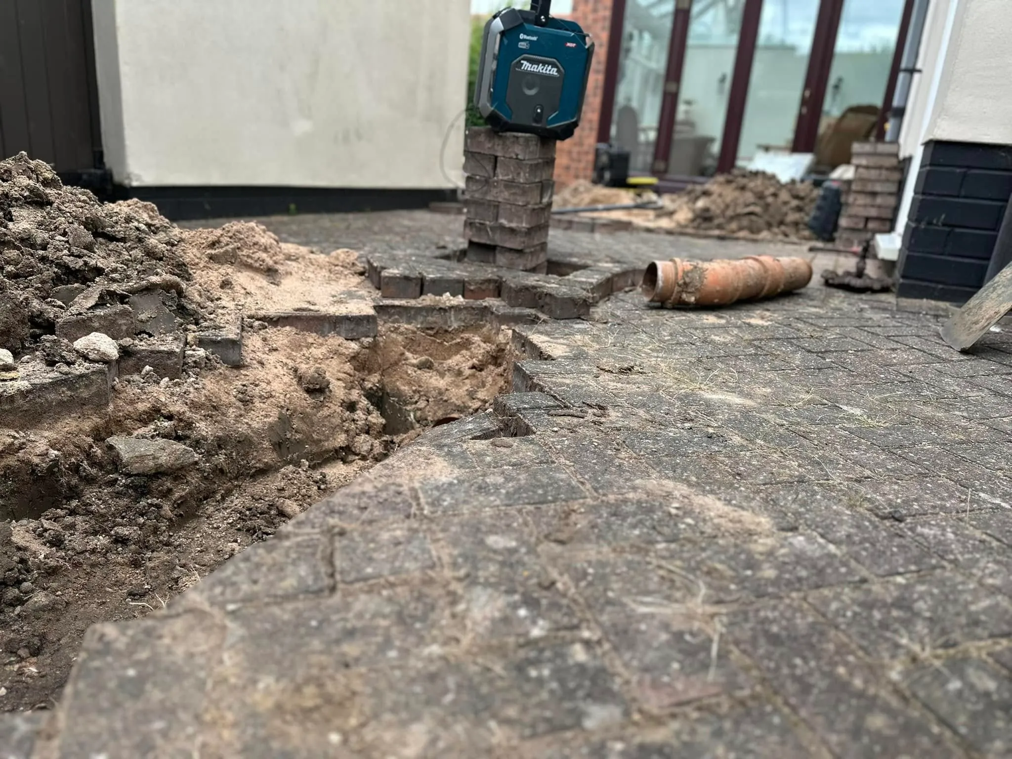 Excavated drain with exposed pipe on a block-paved driveway.