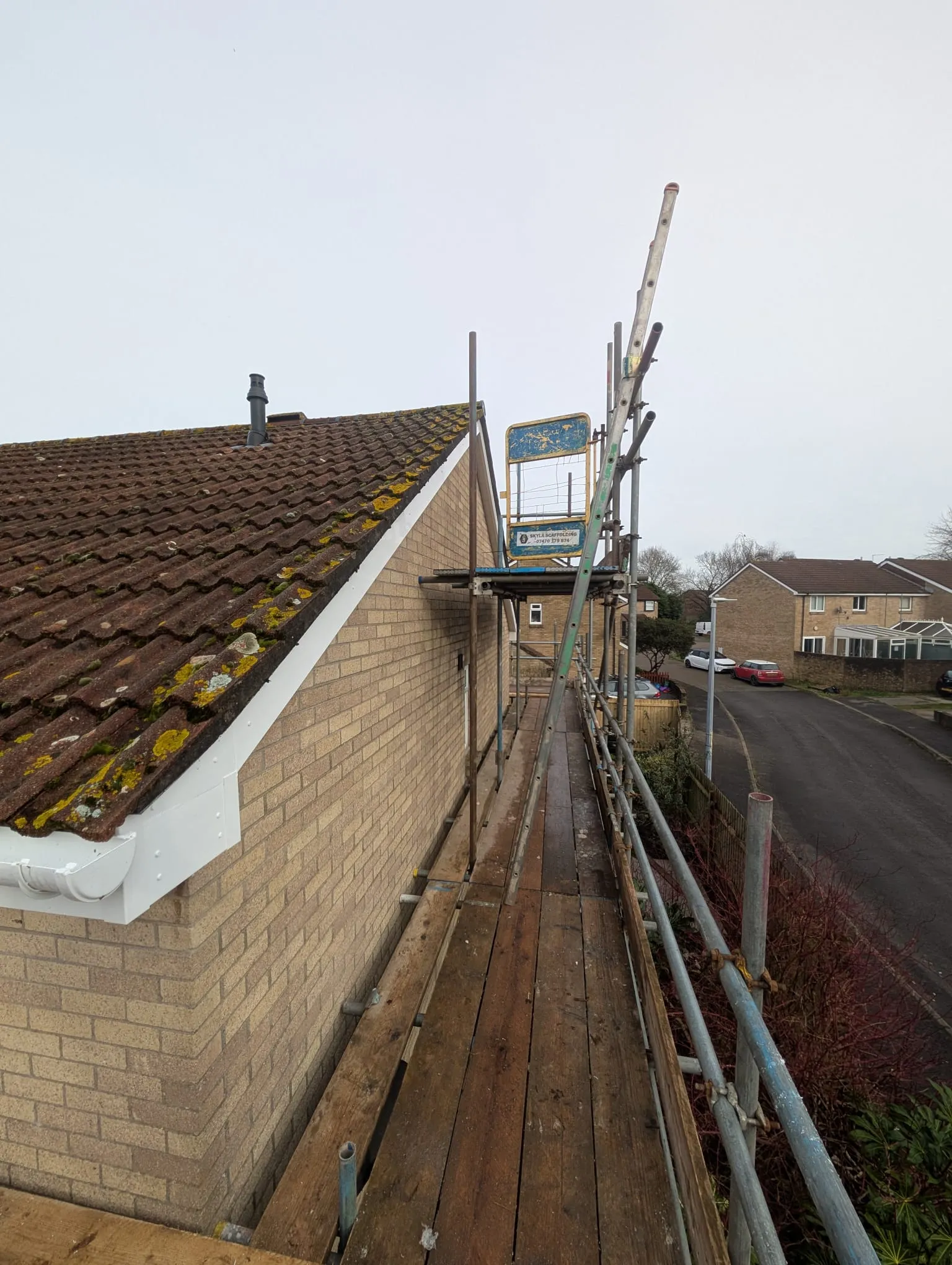 Scaffolding next to a house with a tiled roof, new white gutters, and fascias, seen from above.