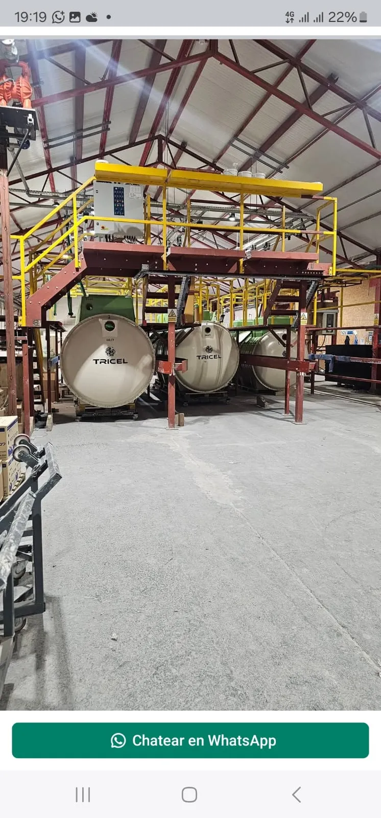 Three large Tricel sewage treatment plant units in a factory or storage facility, highlighting professional installation services.