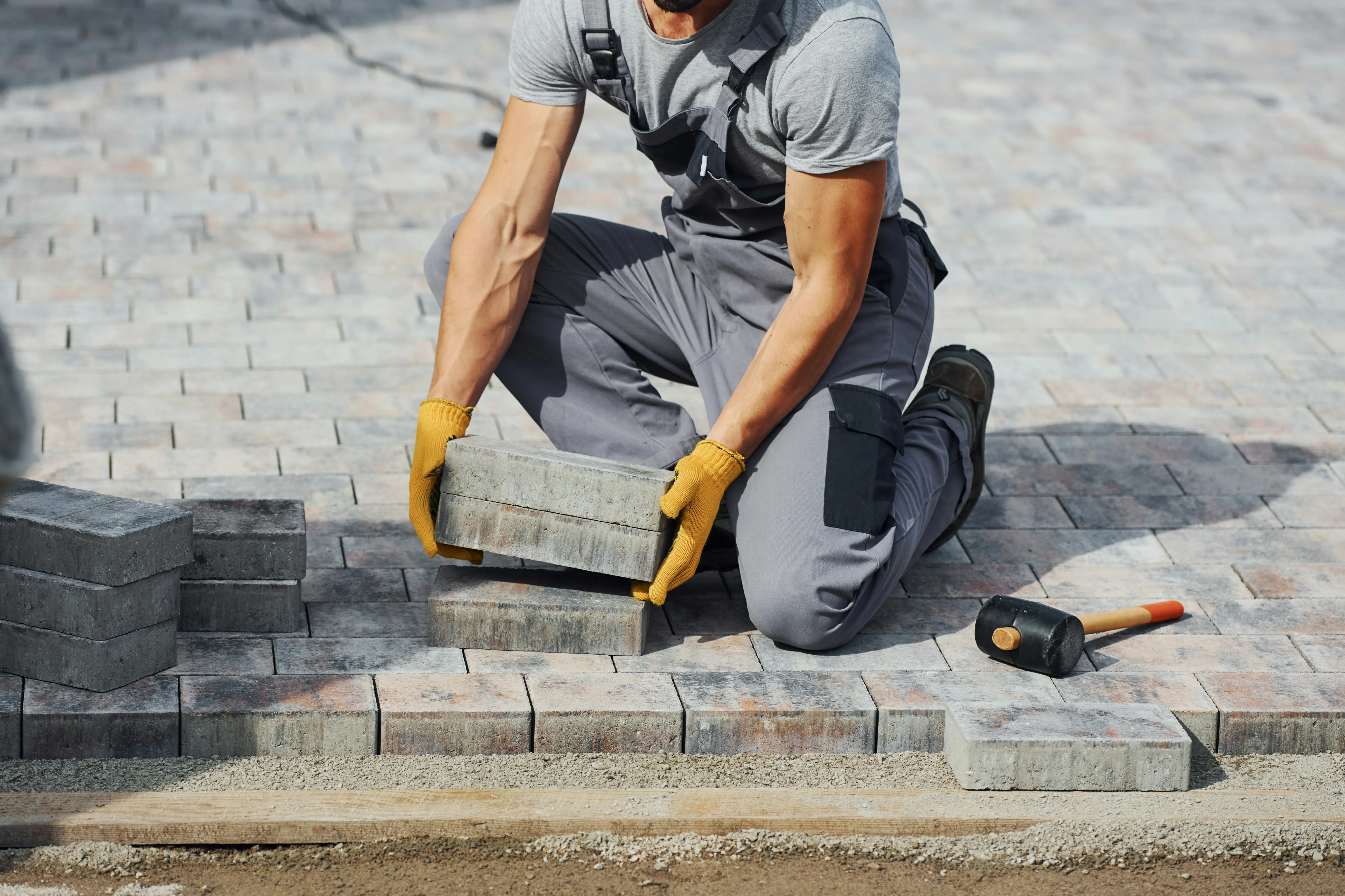Skilled worker laying block paving stones for a new driveway or patio installation in Haywards Heath.