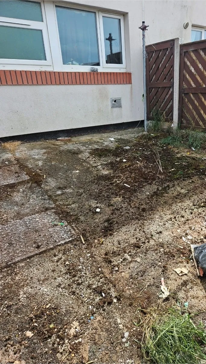 Before clearance: A dirty and unkempt backyard or side yard of a house with scattered rubbish and overgrown patches, ready for a clean-up.