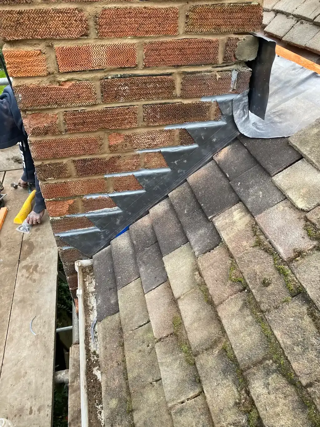 Roofer installing new lead flashing around the base of a brick chimney stack on a tiled roof.
