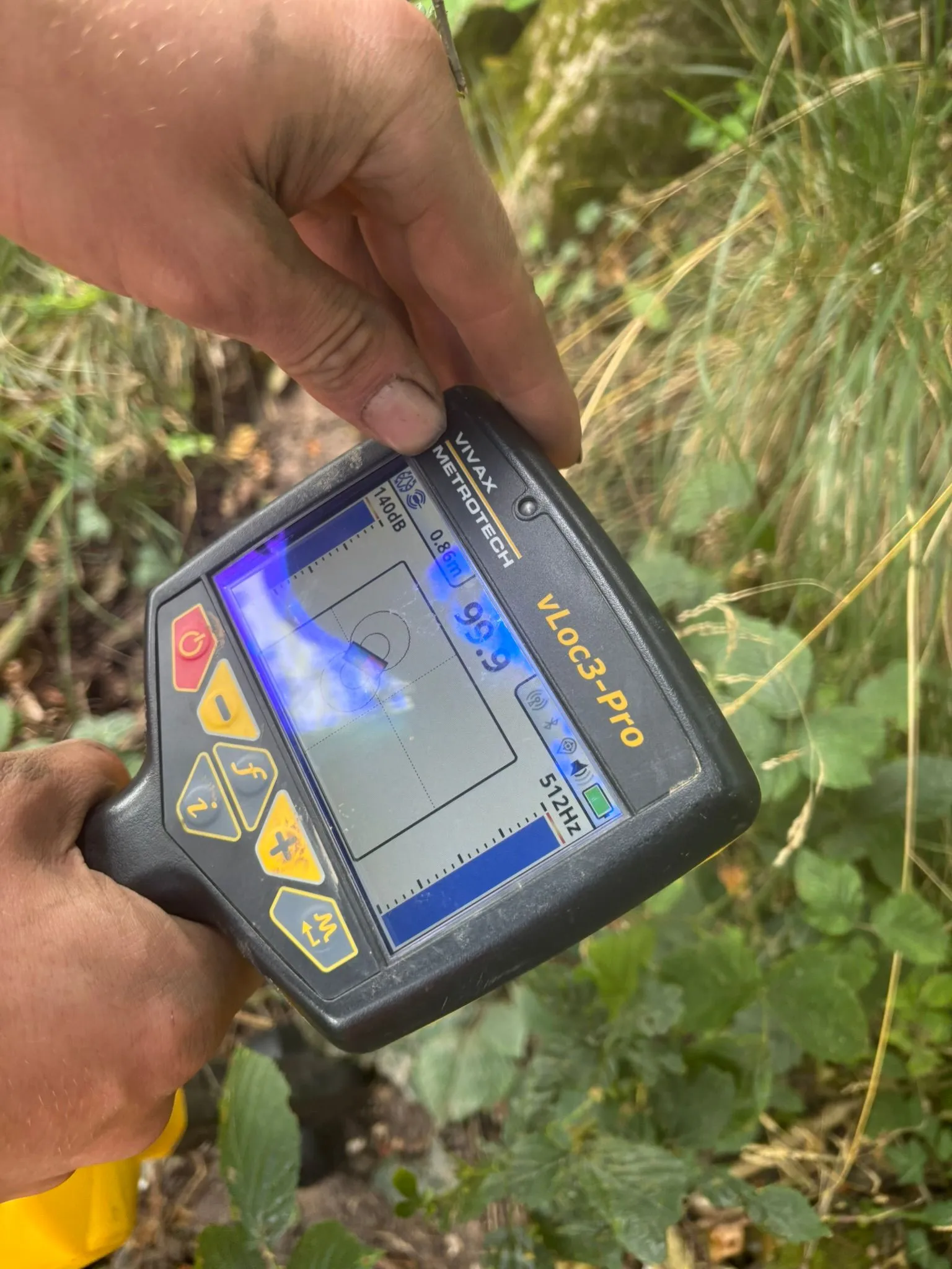 Hand operating a Vivax Metrotech vLoc3-Pro pipe locator for underground drain detection.
