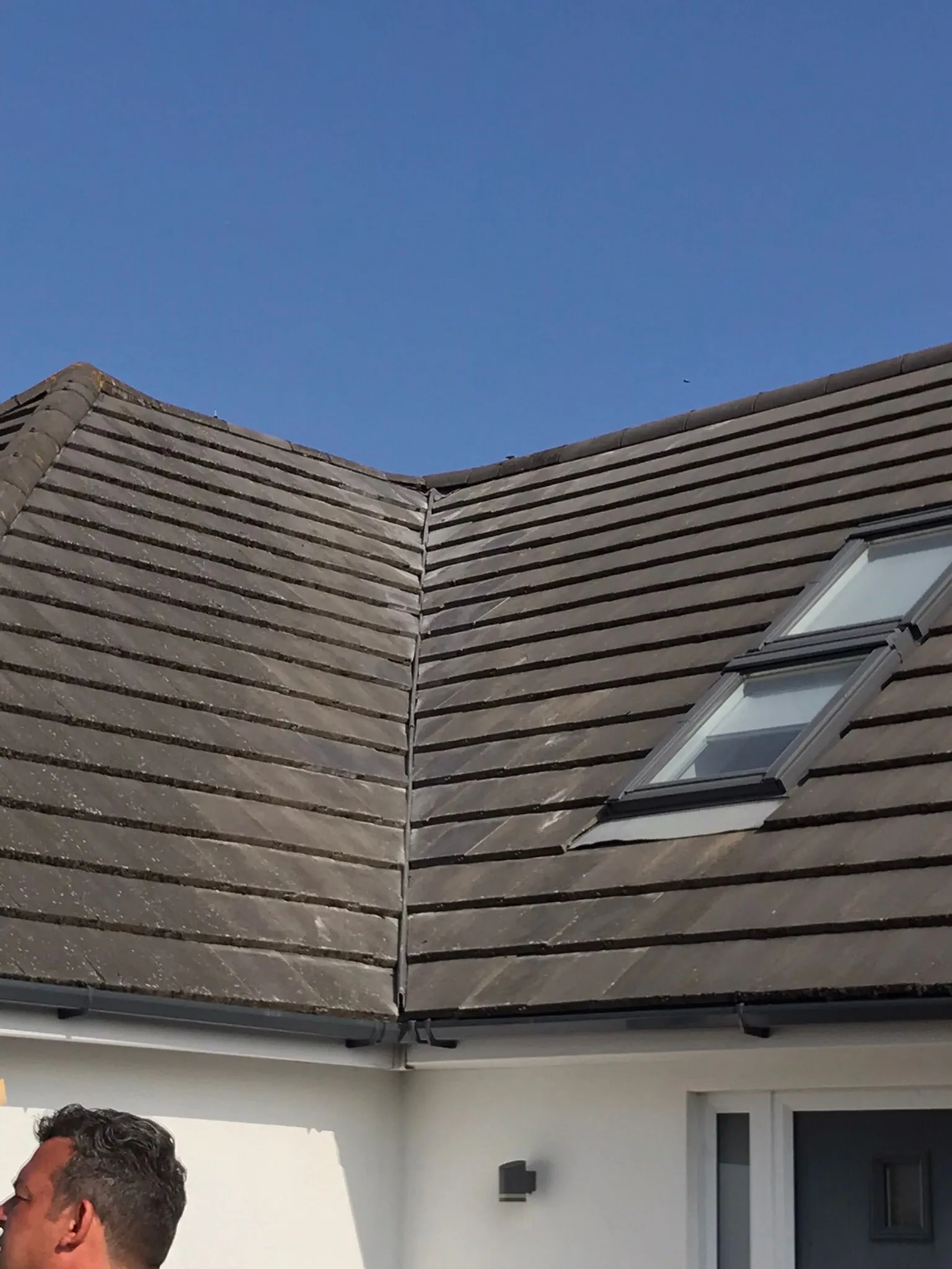 Tiled roof with Velux window and guttering under a blue sky.