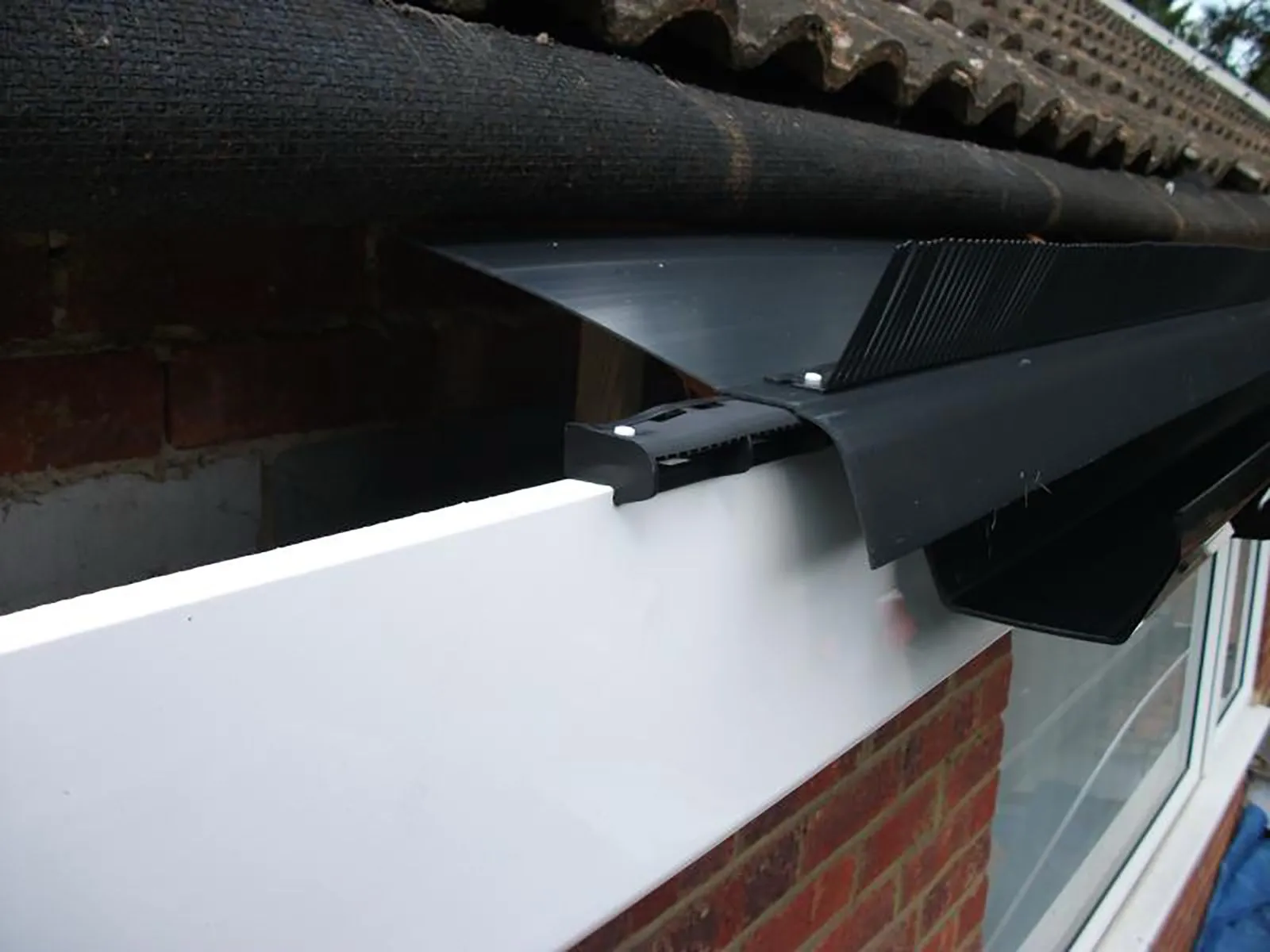 Professional installation of black guttering and white fascia on a house roofline.