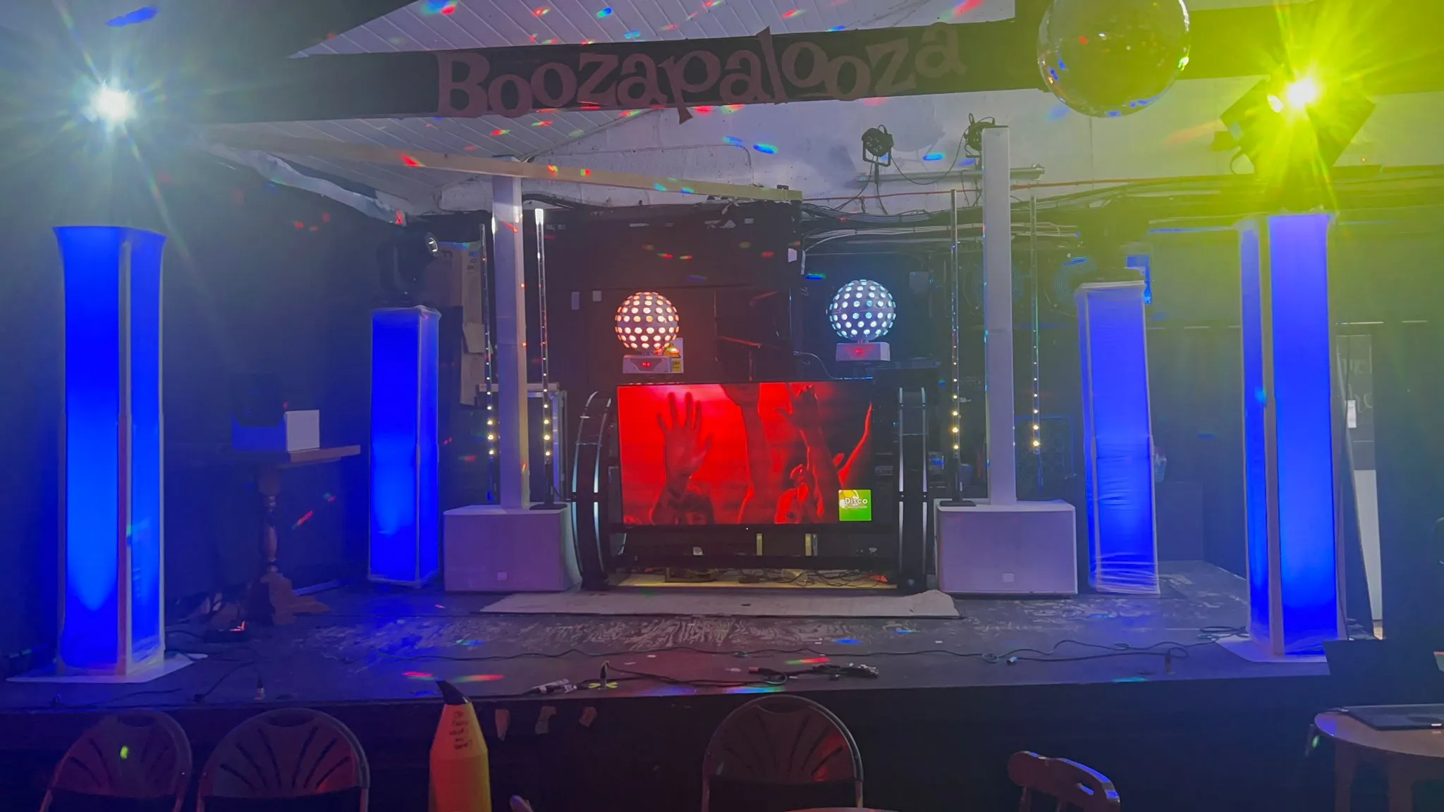 Event stage with full DJ setup, blue uplighting, screen, and disco balls