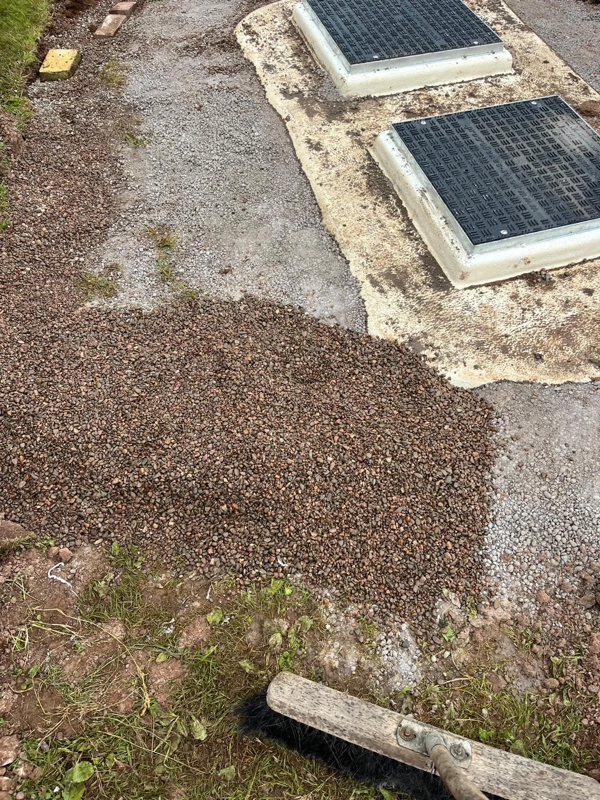 Two dark manhole covers embedded in a gravel and soil area, suggesting an underground drainage or septic system.