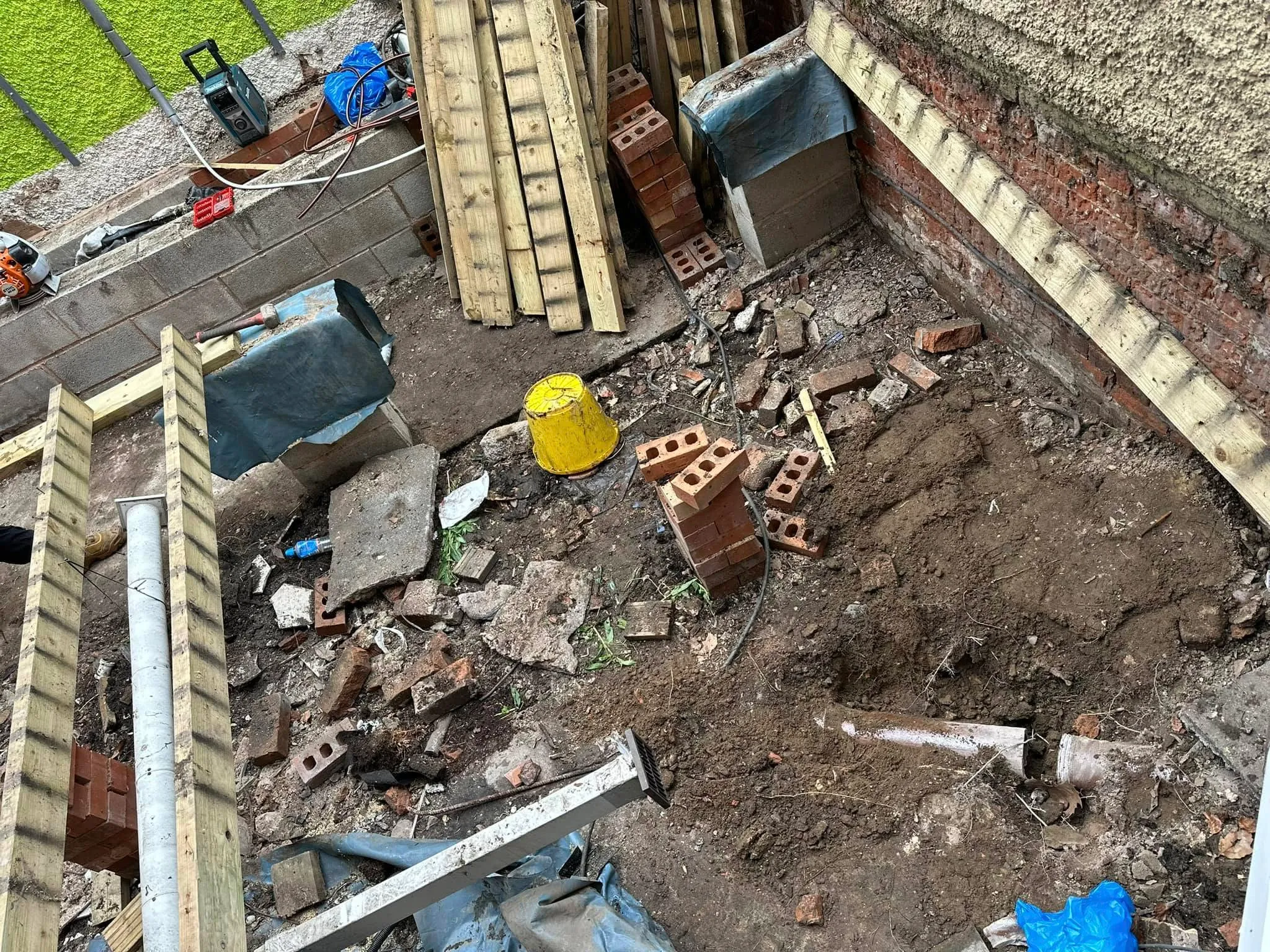 Excavation for drainage installation or repair showing pipes, bricks, and construction debris on a building site.
