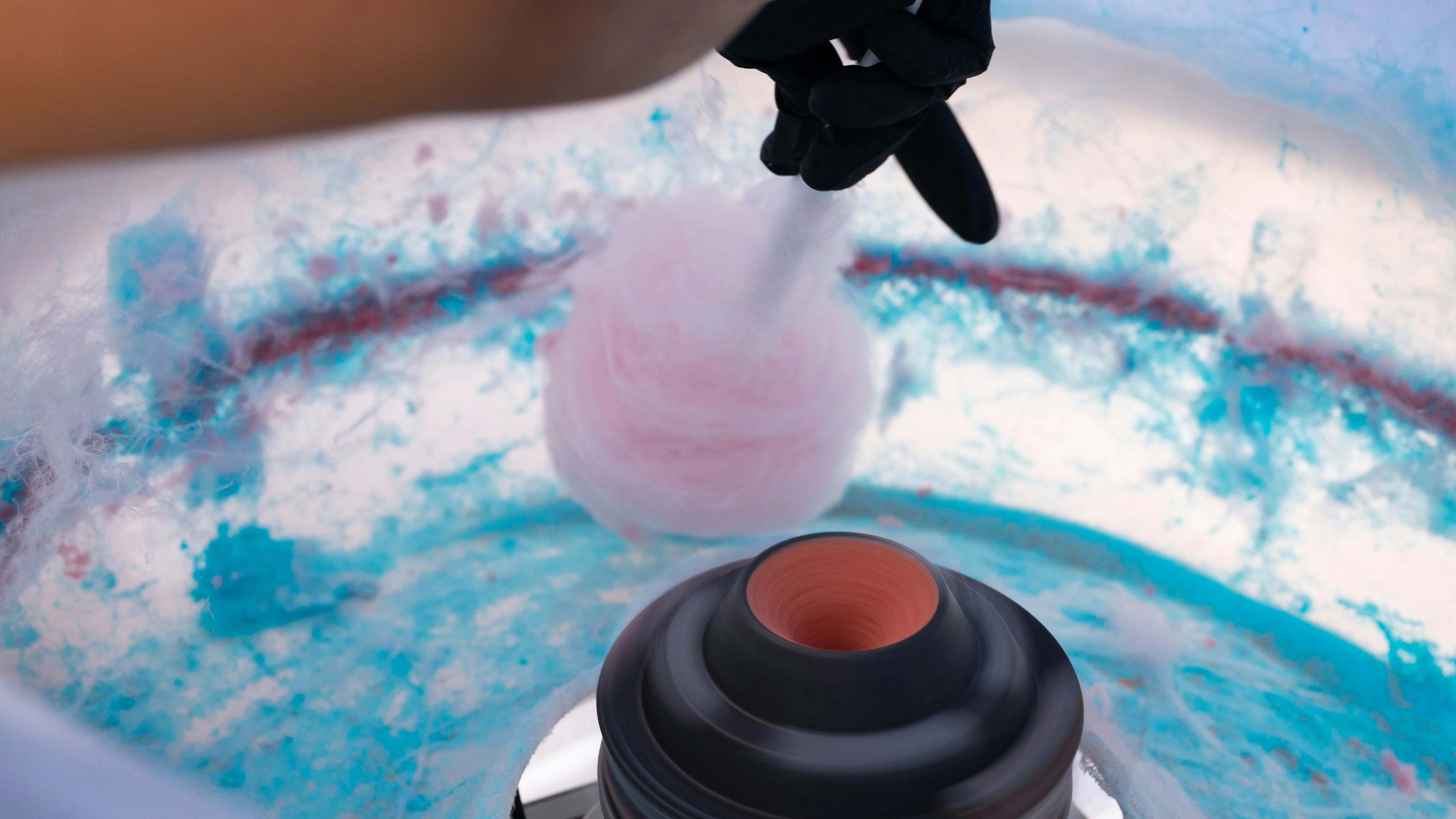 Close-up of a hand in a black glove collecting freshly spun pink candy floss from a machine.