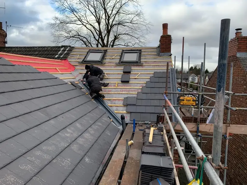 Roofers installing grey roof tiles on a domestic property with scaffolding and velux windows visible.