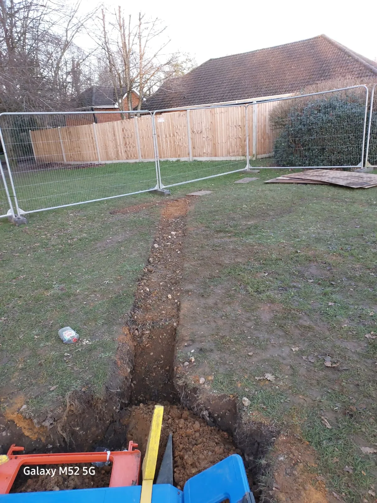An excavated trench for drainage work on a property, with temporary safety fences set up around the site.