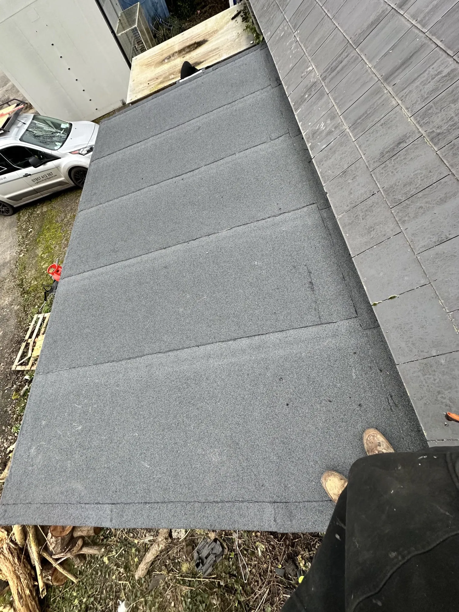 Top-down view of a newly installed grey felt flat roof section meeting a grey tiled pitched roof, showcasing quality workmanship.