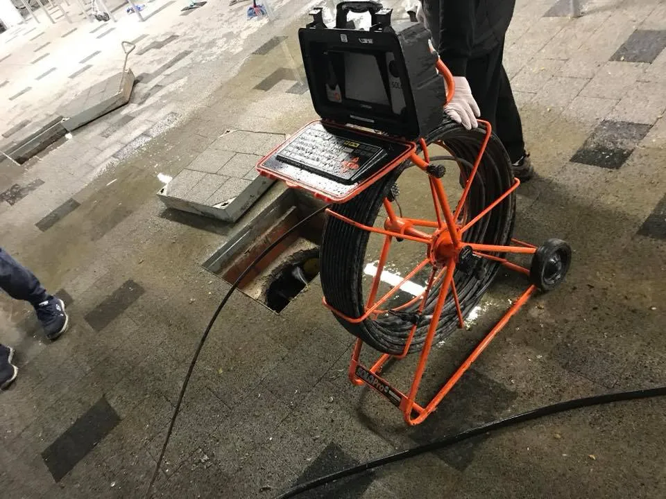 Close-up of CCTV drain survey equipment with a camera cable extending into an open drain access.