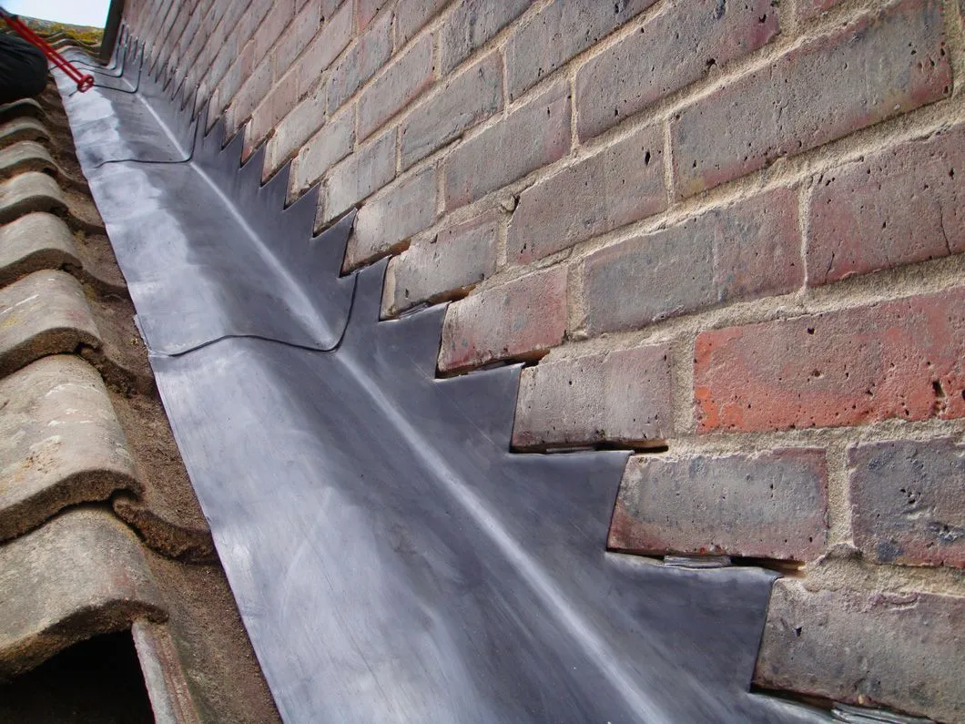 New lead flashing installed on a roof against a brick wall