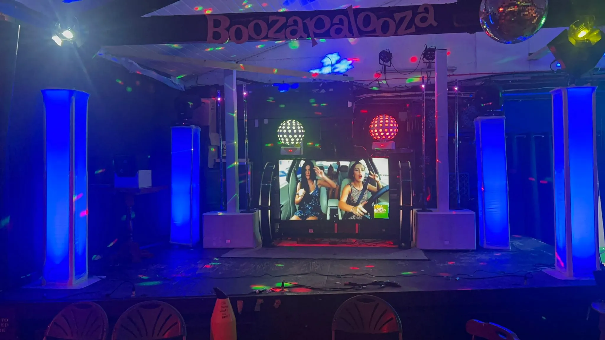 Professional DJ setup with blue uplighting, large screen for music videos, and disco lights on a stage, ready for a party.