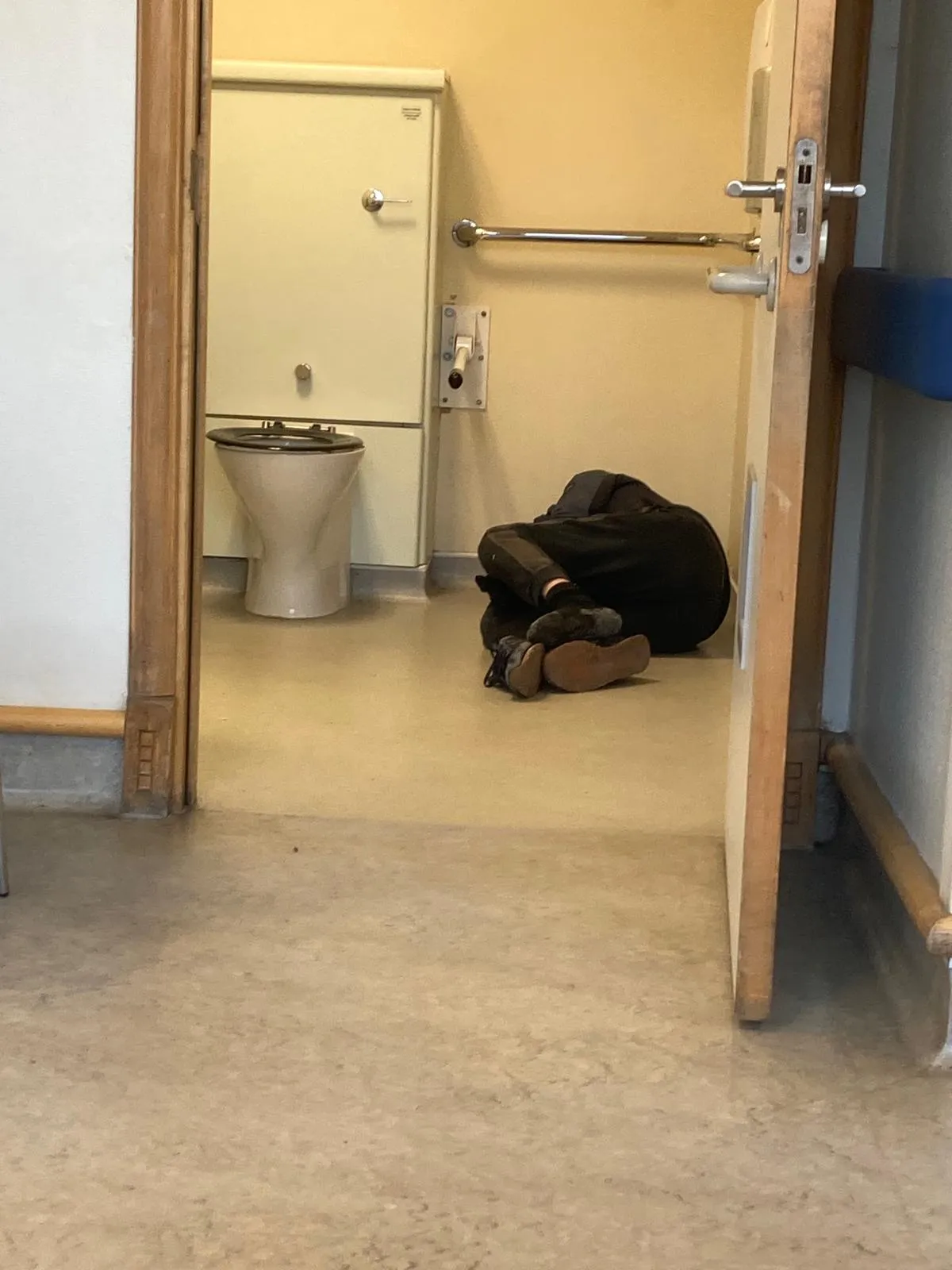 A public restroom with a toilet and a person lying on the floor.