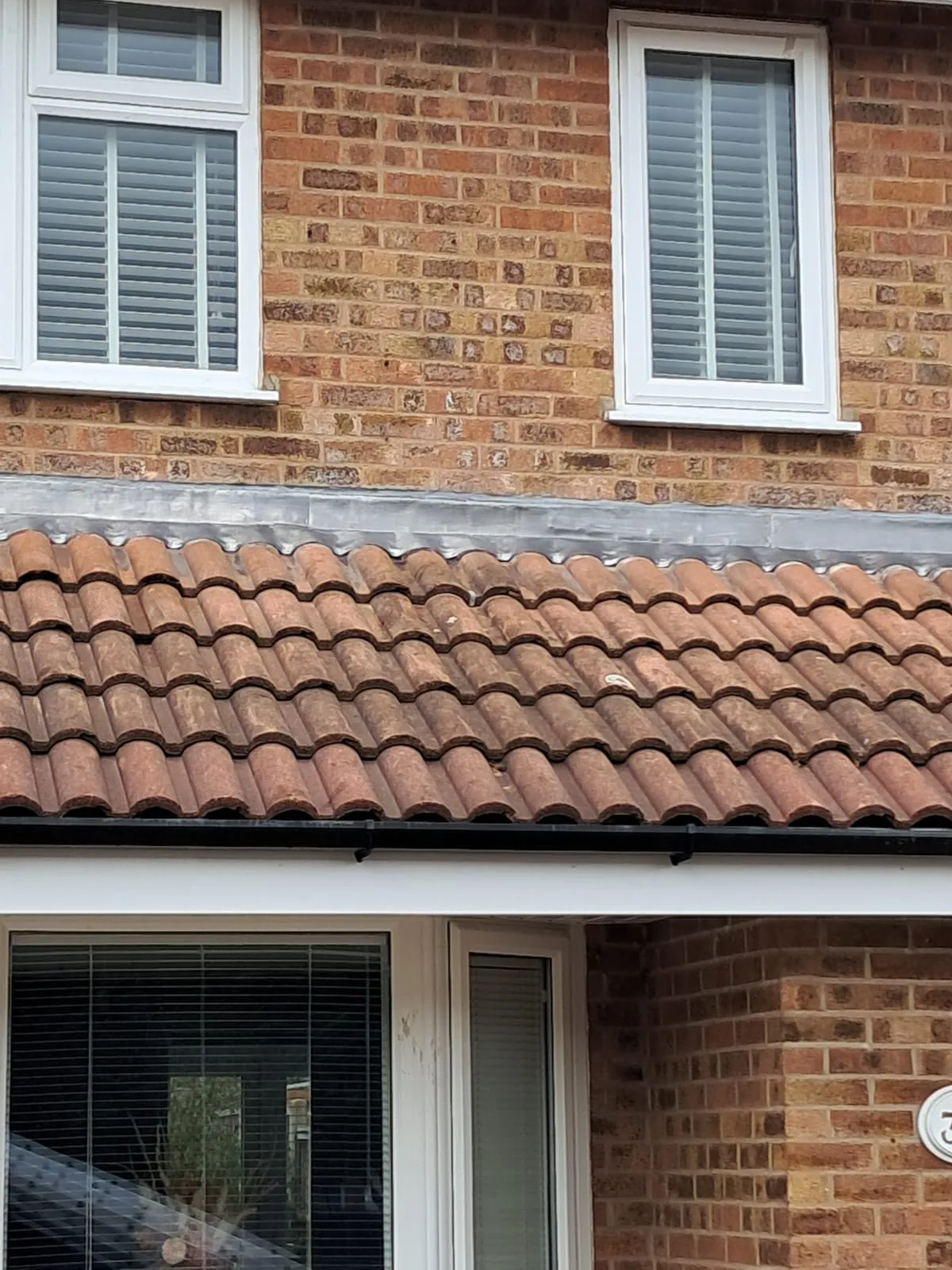 Tiled roof with red tiles, lead flashing, white fascias, soffits, and black guttering on a brick residential house in Leicestershire.