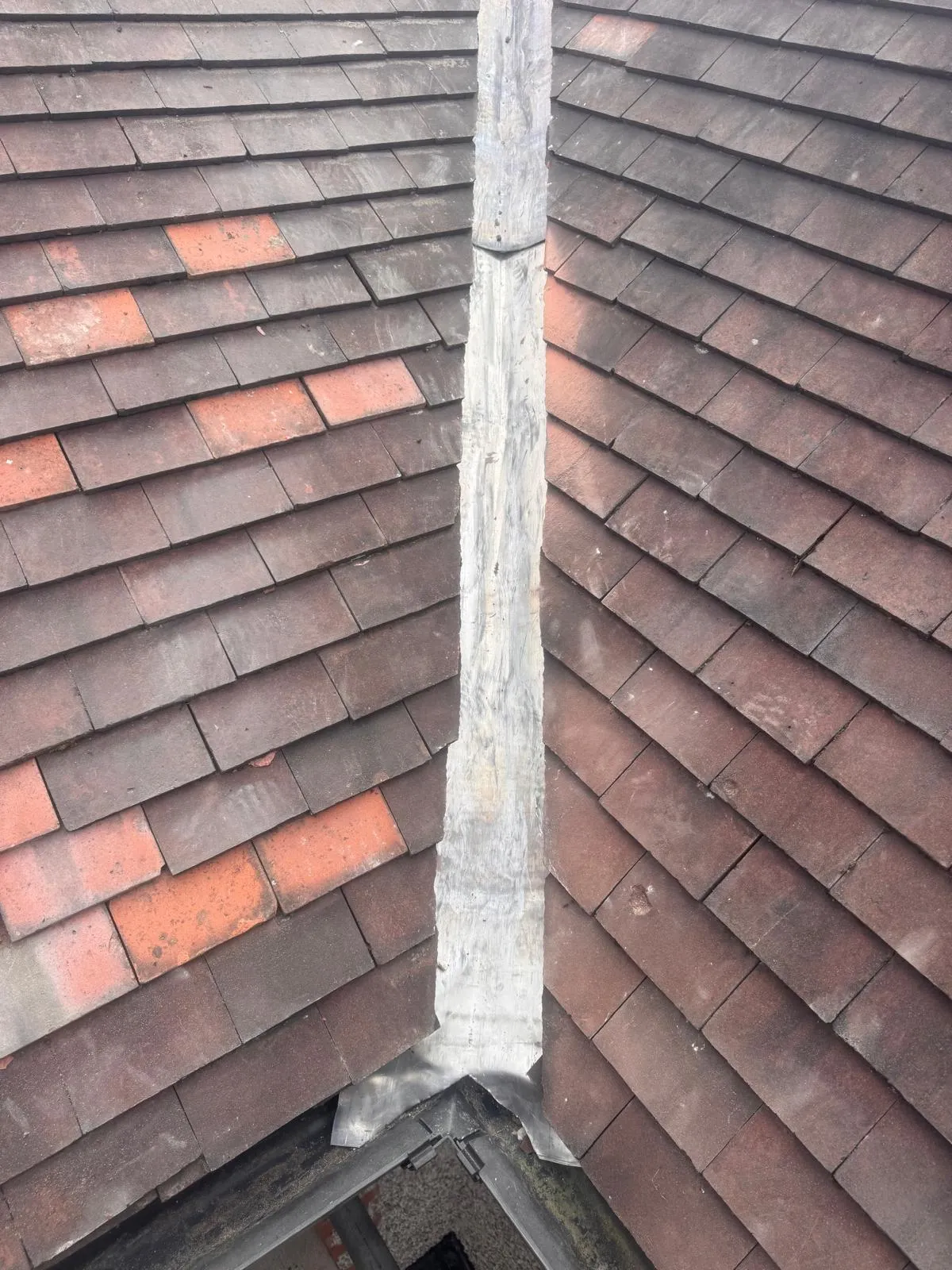 Close-up of a weathered tiled roof valley with lead flashing, suitable for roof repair or leadwork services.
