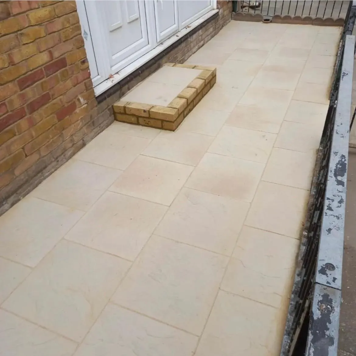 Newly laid patio with light beige paving slabs and a low brick step leading to a house entrance.