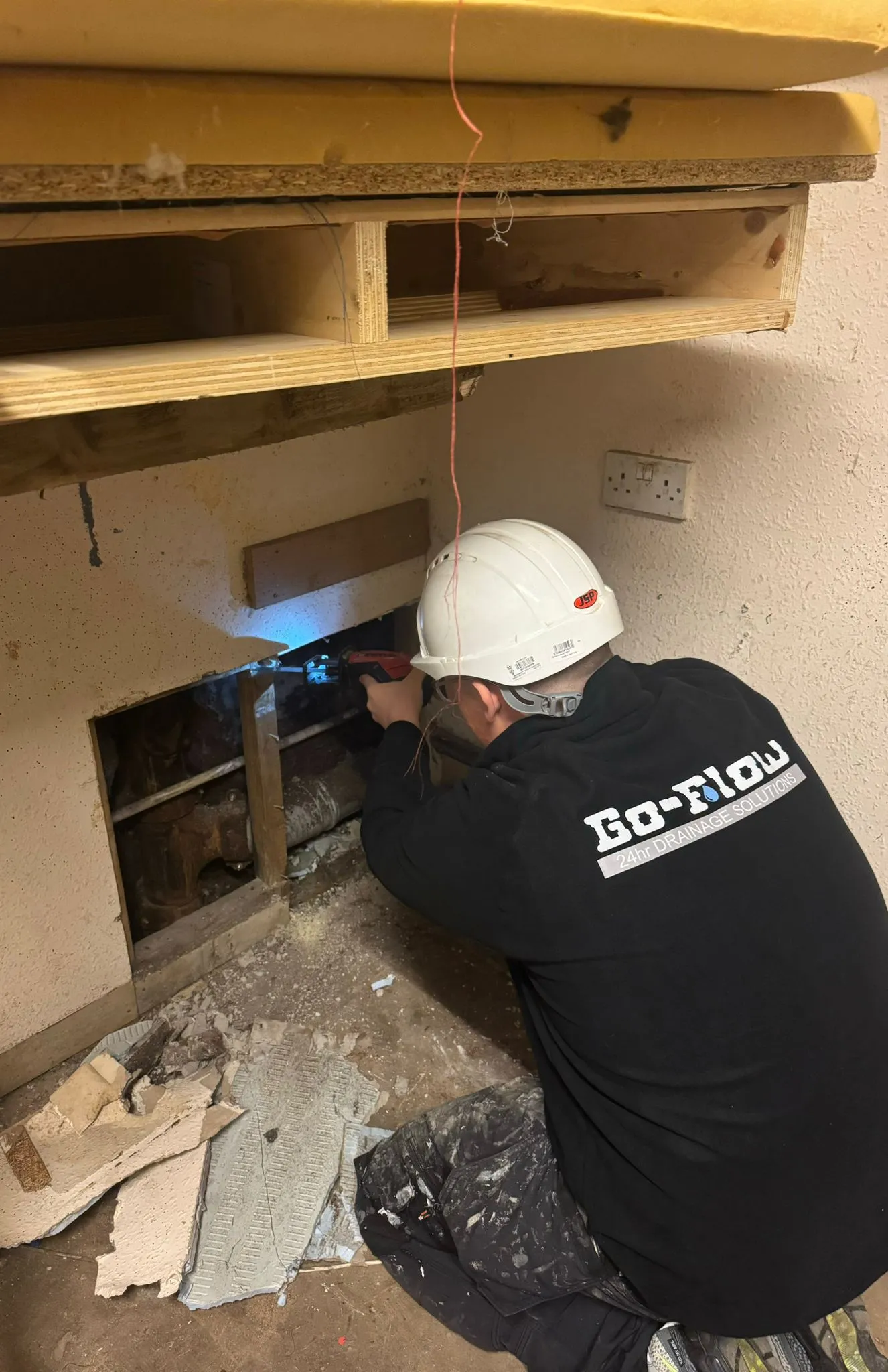Go-Flow engineer using a reciprocating saw to access drainage pipes behind a wall.