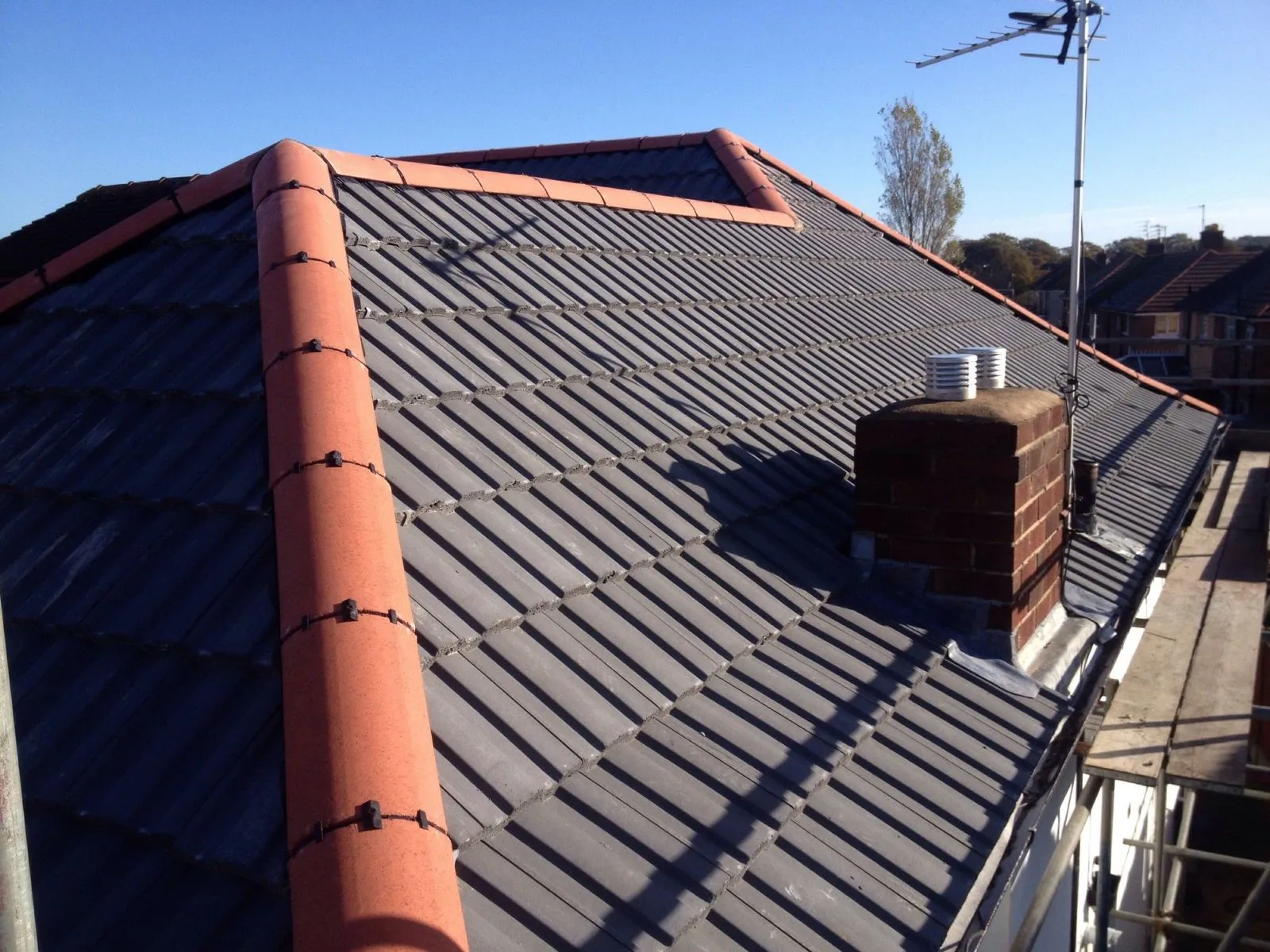 Newly installed grey tiled roof with red ridge tiles and chimney