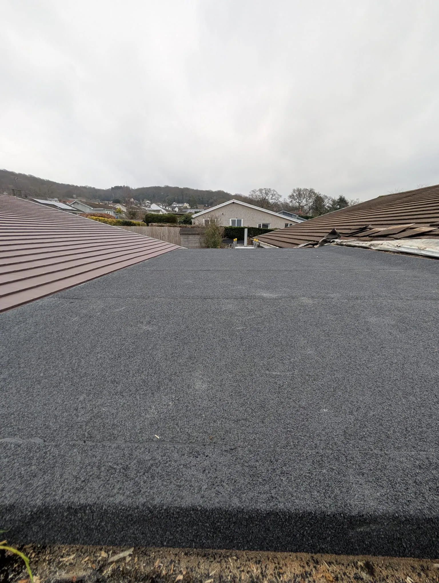 A new flat roof installation next to a section of a brown tiled pitched roof on a residential property.