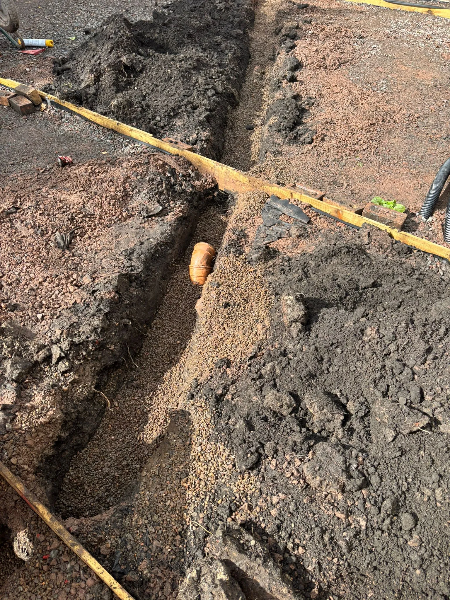 An orange drainage pipe in an open trench, surrounded by gravel and excavated earth, ready for installation or repair.
