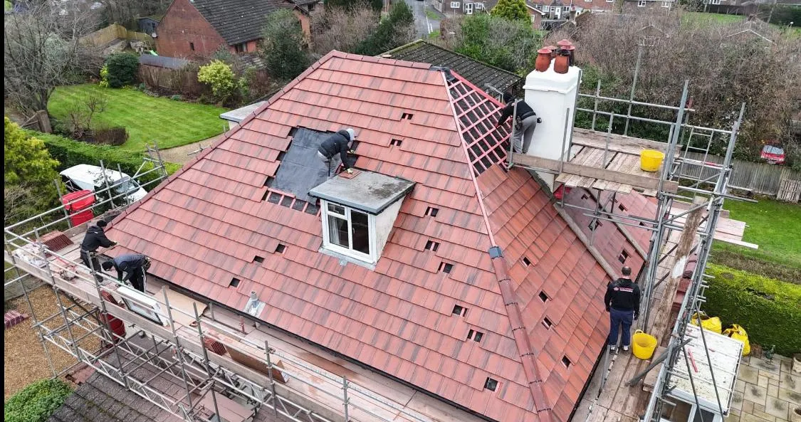 Professional roofers installing new tiles on a house roof during a complete re-roofing project, with scaffolding erected.