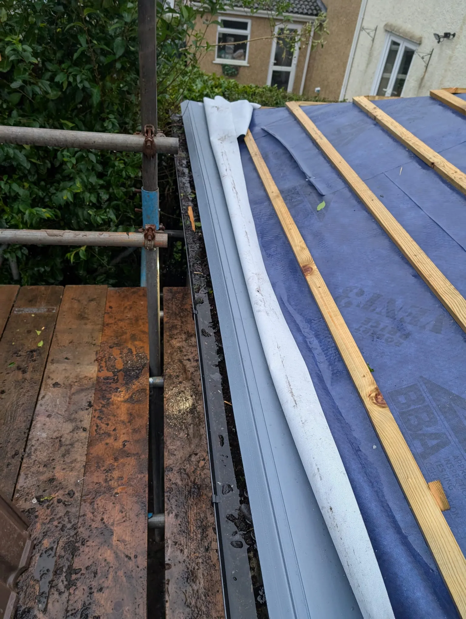 New roof installation in progress on a residential property, showing a blue breathable membrane, wooden battens, and scaffolding.