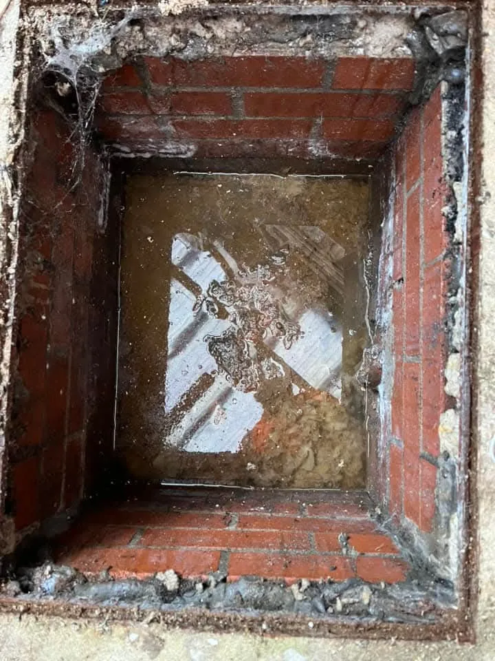 An overflowing drainage manhole filled with murky water and debris.