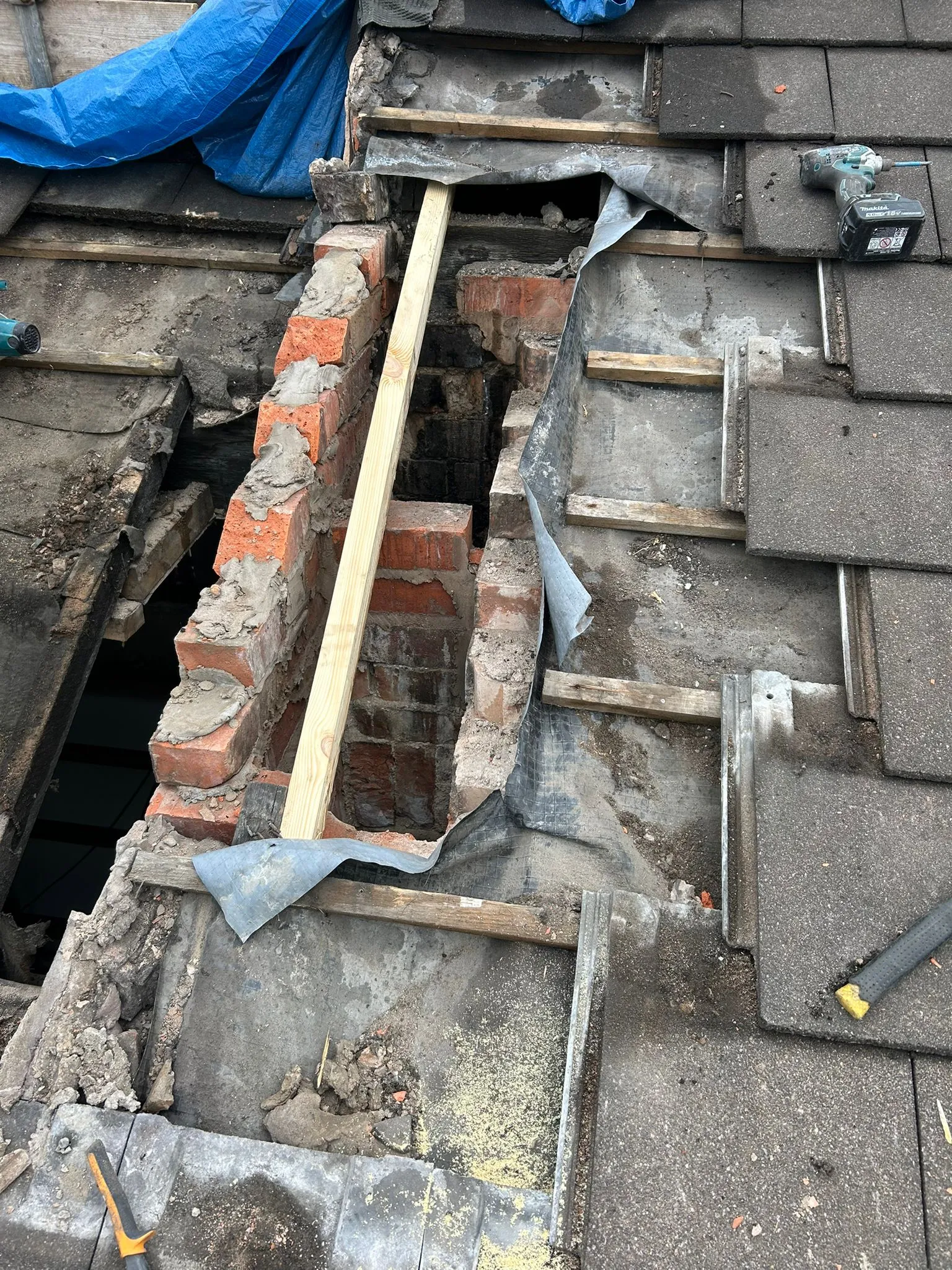 Roof repair in progress, focusing on exposed chimney brickwork and surrounding roof structure