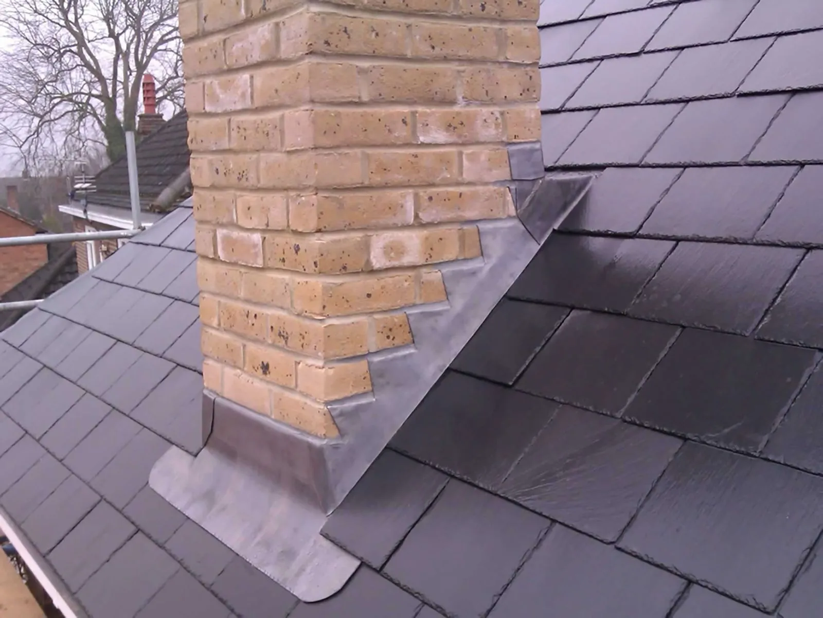 Professional lead flashing installed around a brick chimney stack on a tiled roof in Haywards Heath.