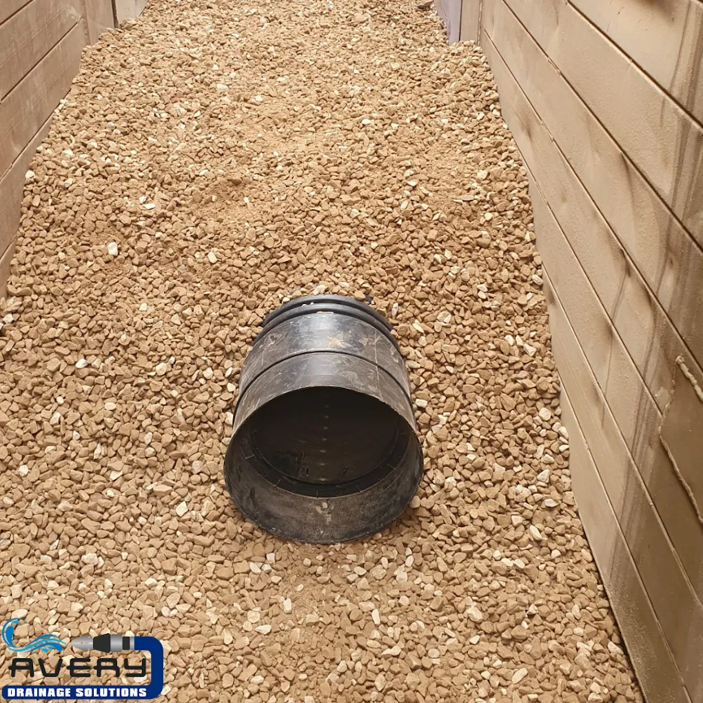 Drainage pipe being installed in a gravel trench for a new drainage system installation.