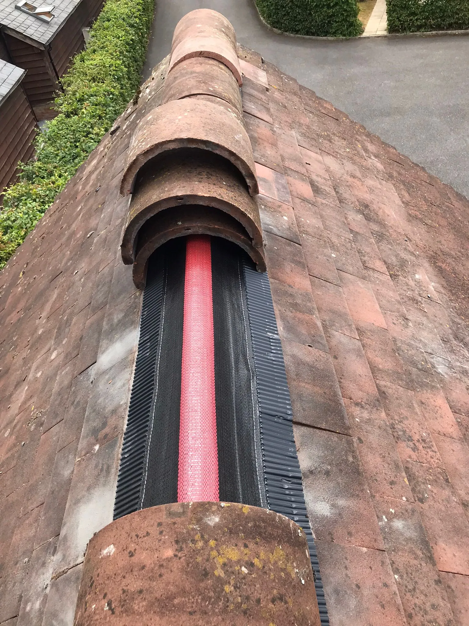 Terracotta tiled roof with a newly installed red and black dry-fix ridge system for ventilation and weather protection.