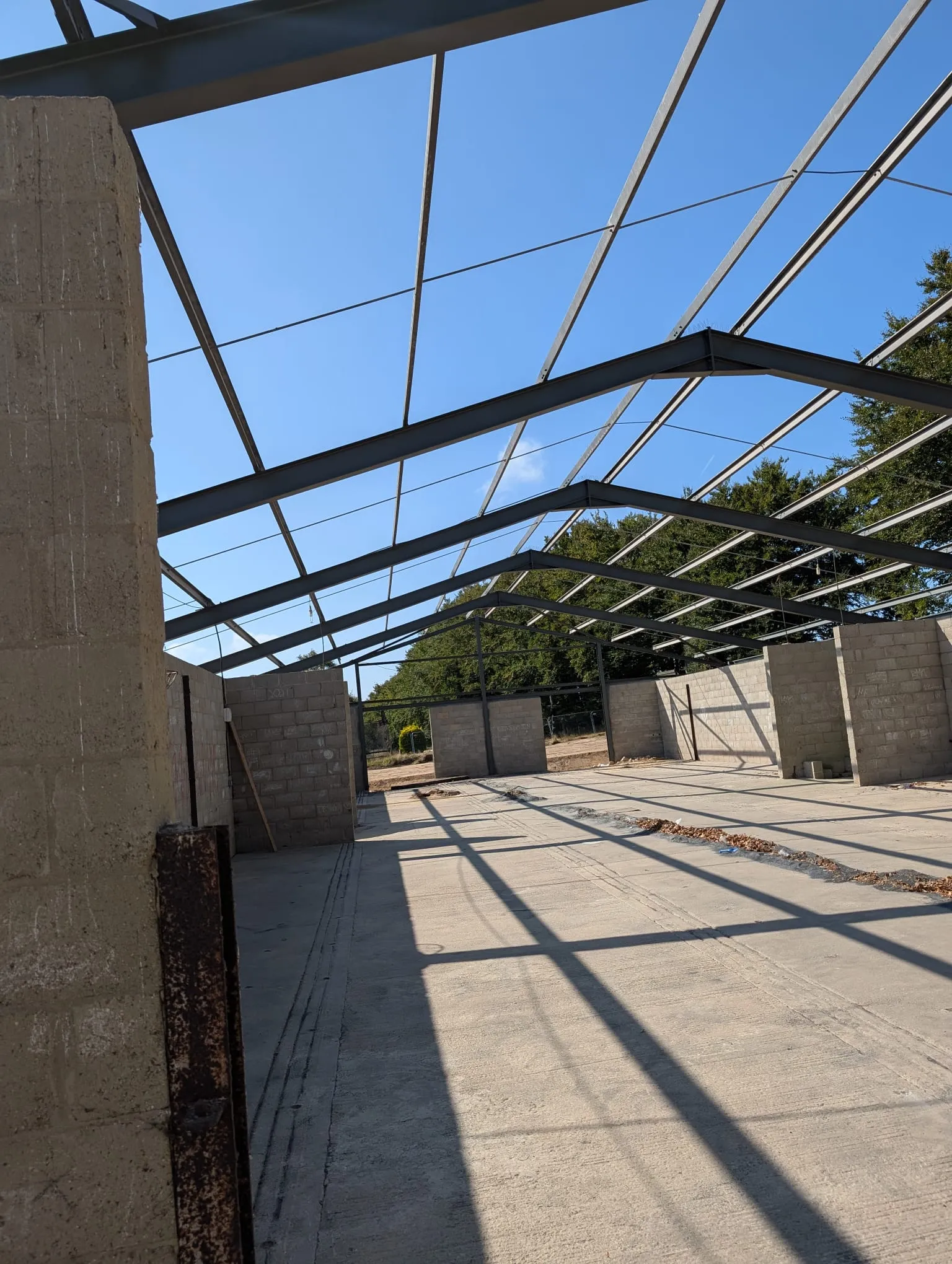 Interior of an industrial building under construction, showcasing its steel roof frame and blockwork walls, ready for further development.