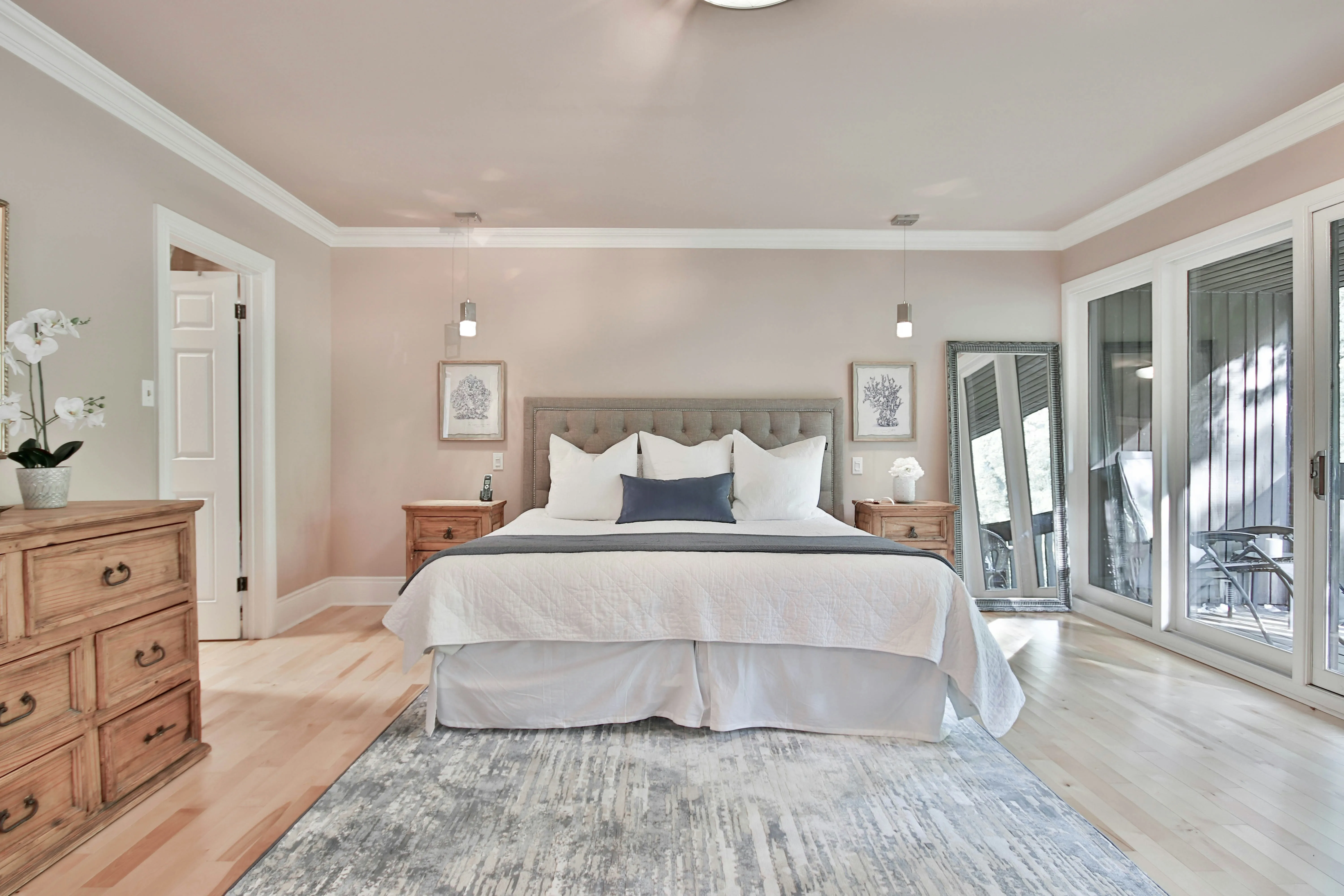 A bright and spacious master bedroom with light wooden floors, a large bed, and a balcony door.