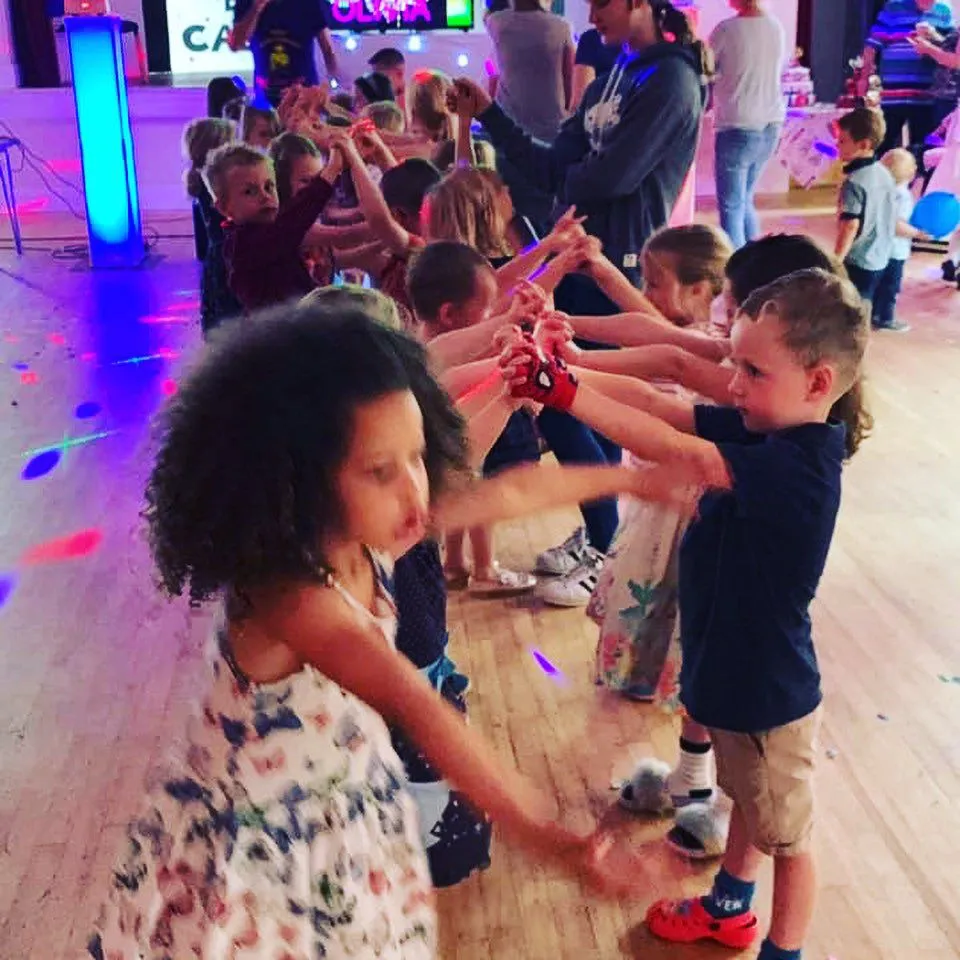 Children dancing and playing at a lively disco party with colourful lights, likely hosted by a DJ.