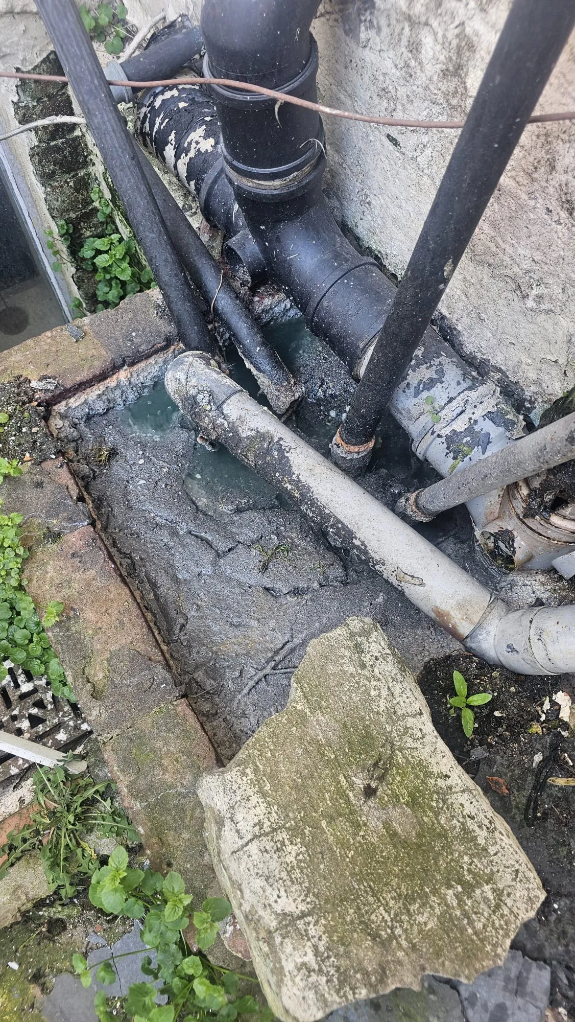 A close-up of a severely blocked outdoor drain overflowing with dirty water and sludge.