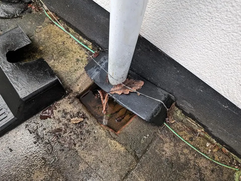 Blocked outdoor drain overflowing with water and debris.