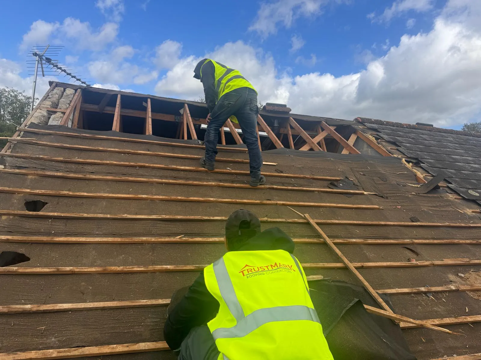 Trustmark Roofing contractors installing new battens and underlayment on a pitched roof, preparing for new tiles or slates.