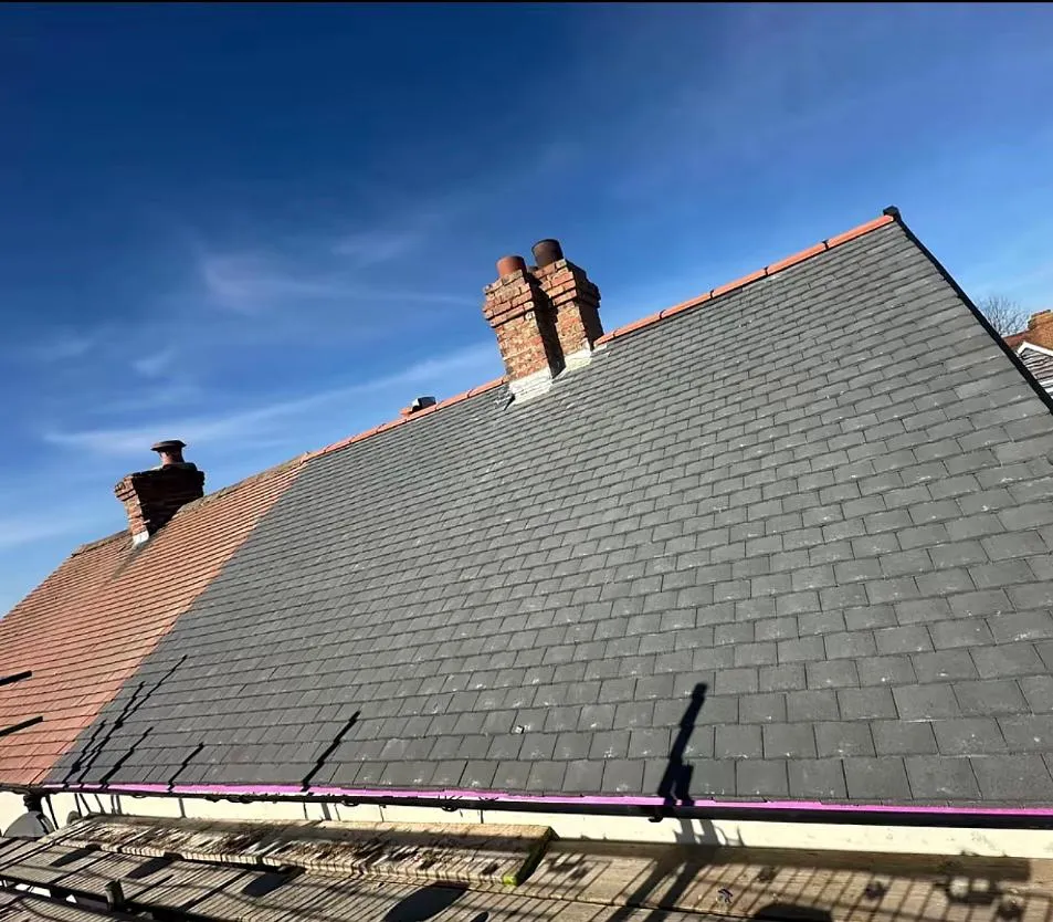 New dark grey slate or tile roof installation in progress on a residential property in Devon or Cornwall, with visible chimneys and scaffolding.