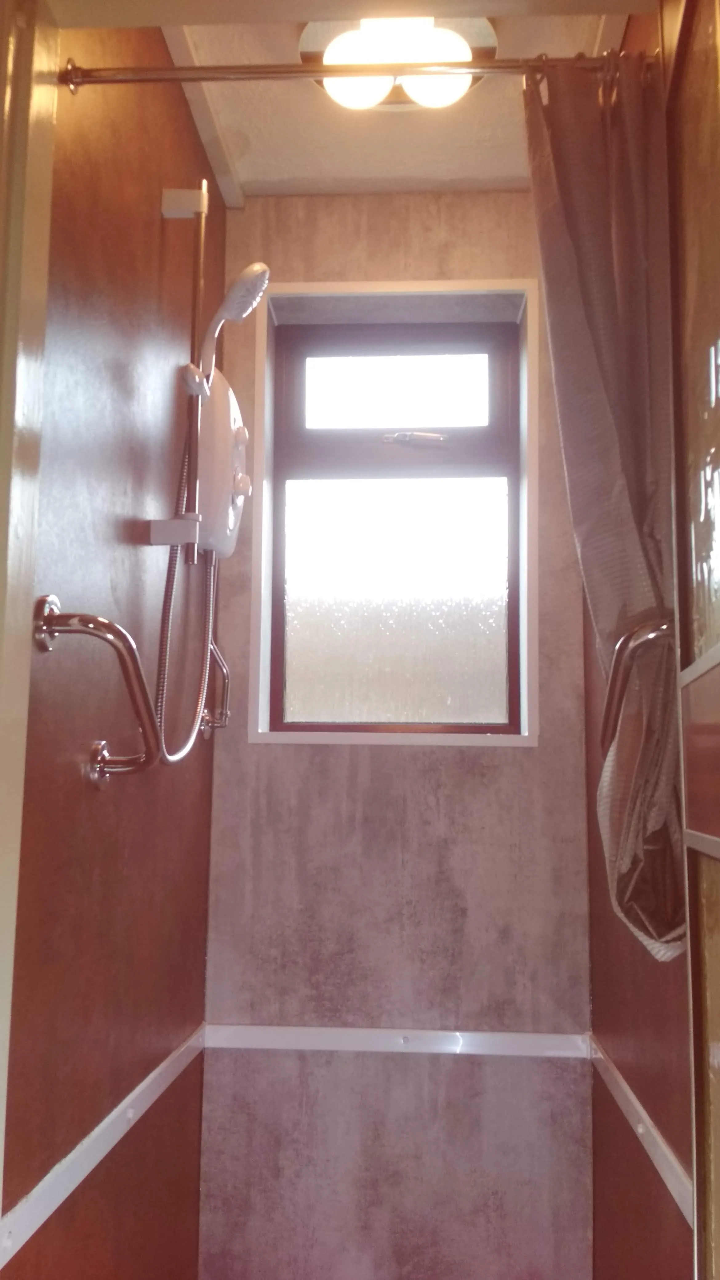 A modern shower installation with an electric shower, grab handle, and window, demonstrating quality plumbing work.
