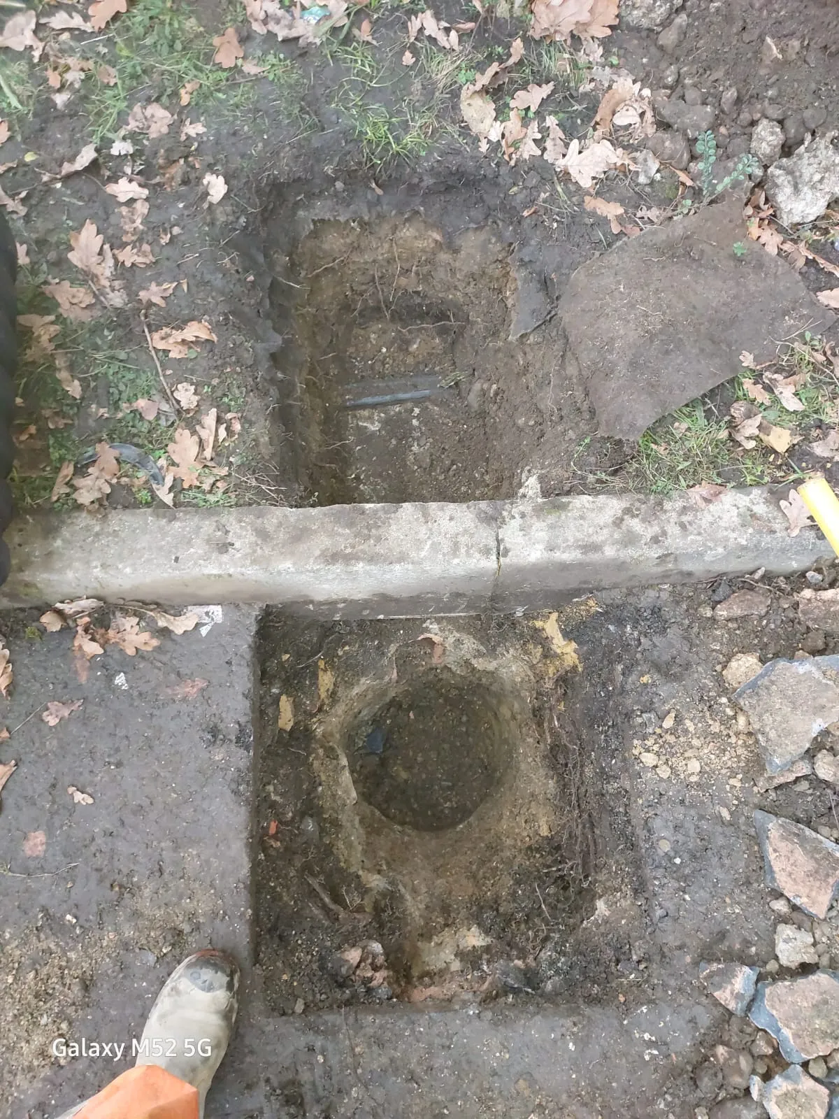 Ground dug up for drainage repair or new installation, with exposed pipes and a concrete kerb.